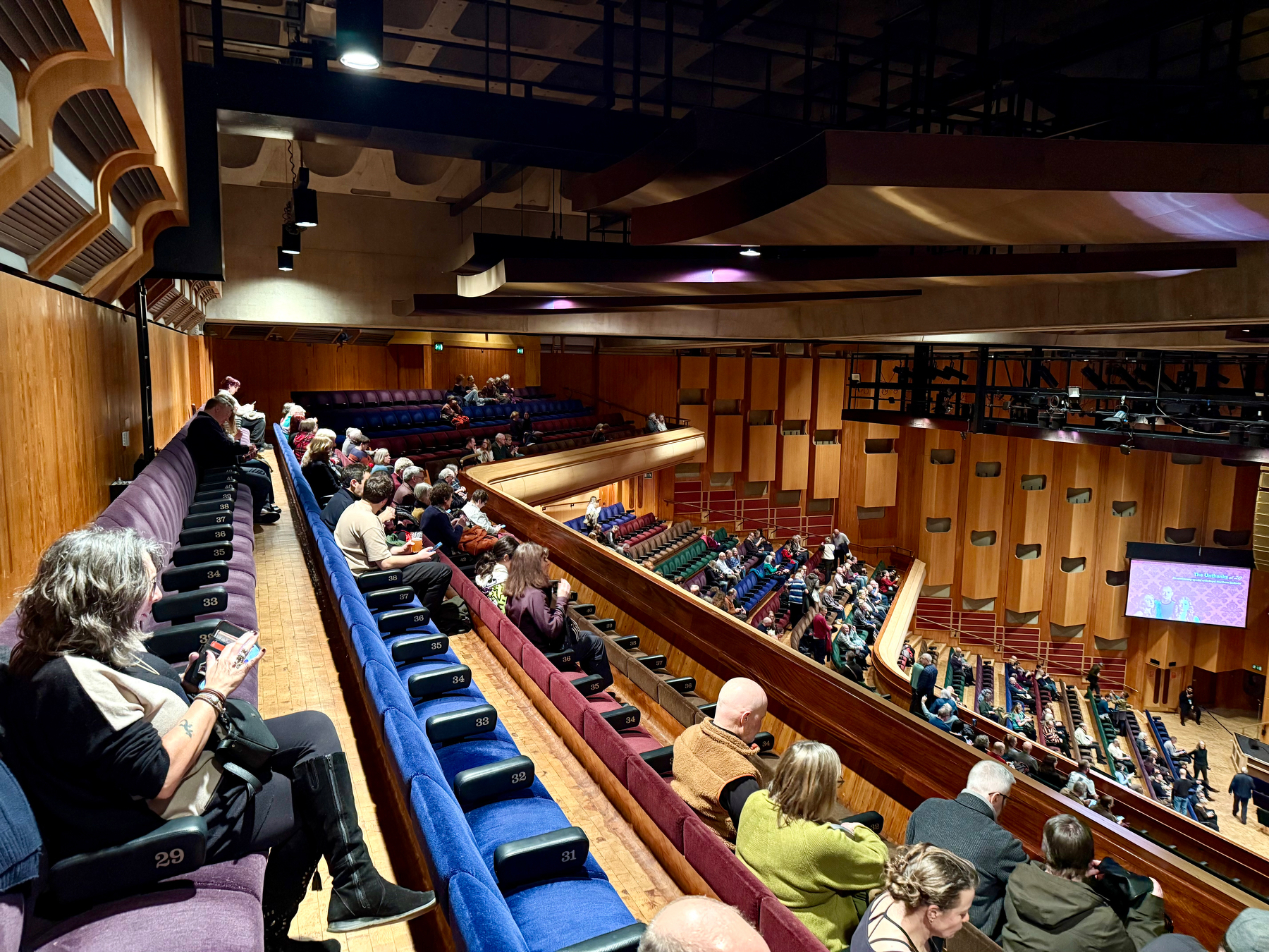 Auto-generated description: People are seated in the upper balcony of a concert hall, waiting for a performance to begin.