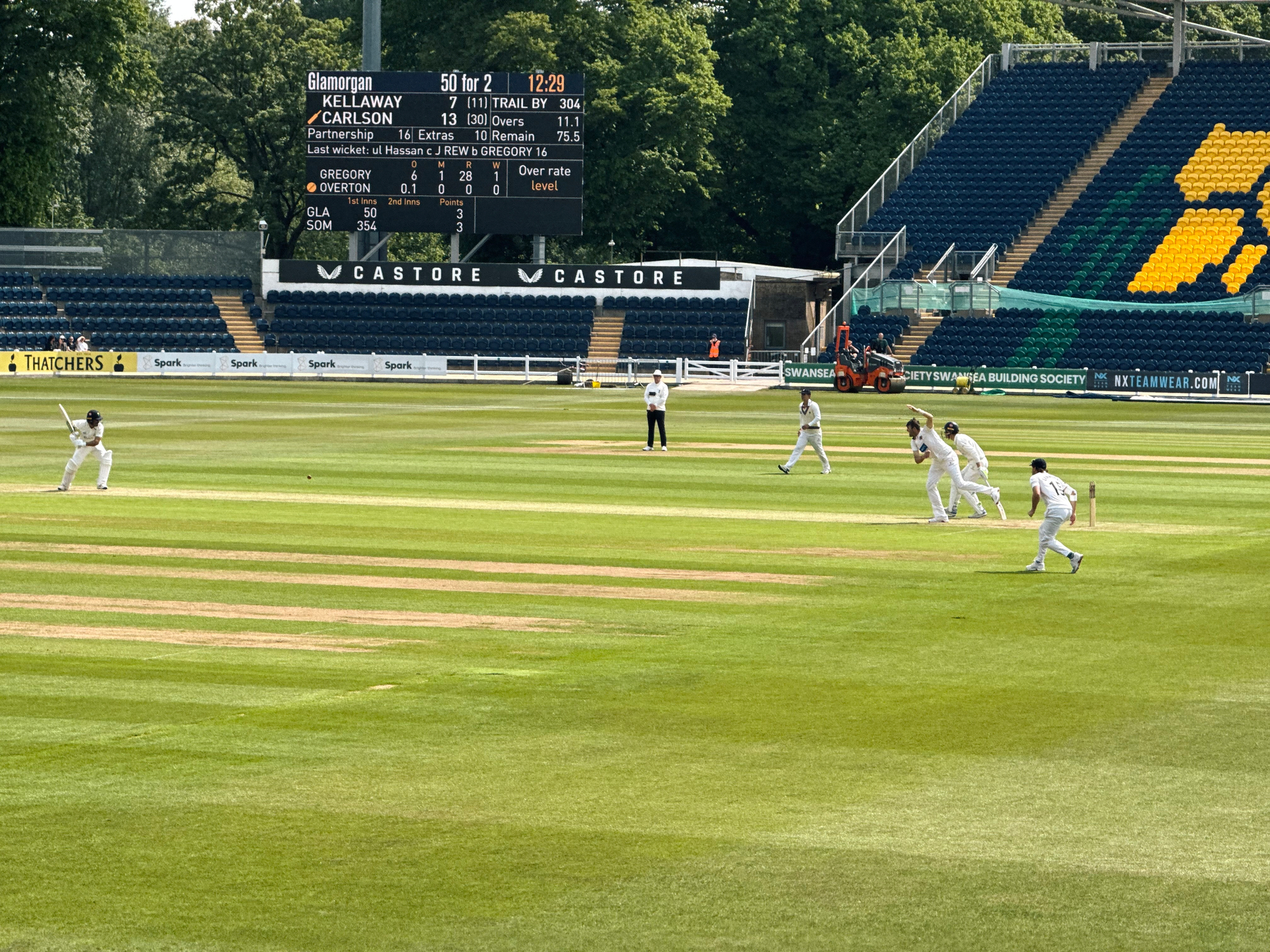 Cricket players are engaged in a match on a well-maintained field with spectators in the stands.